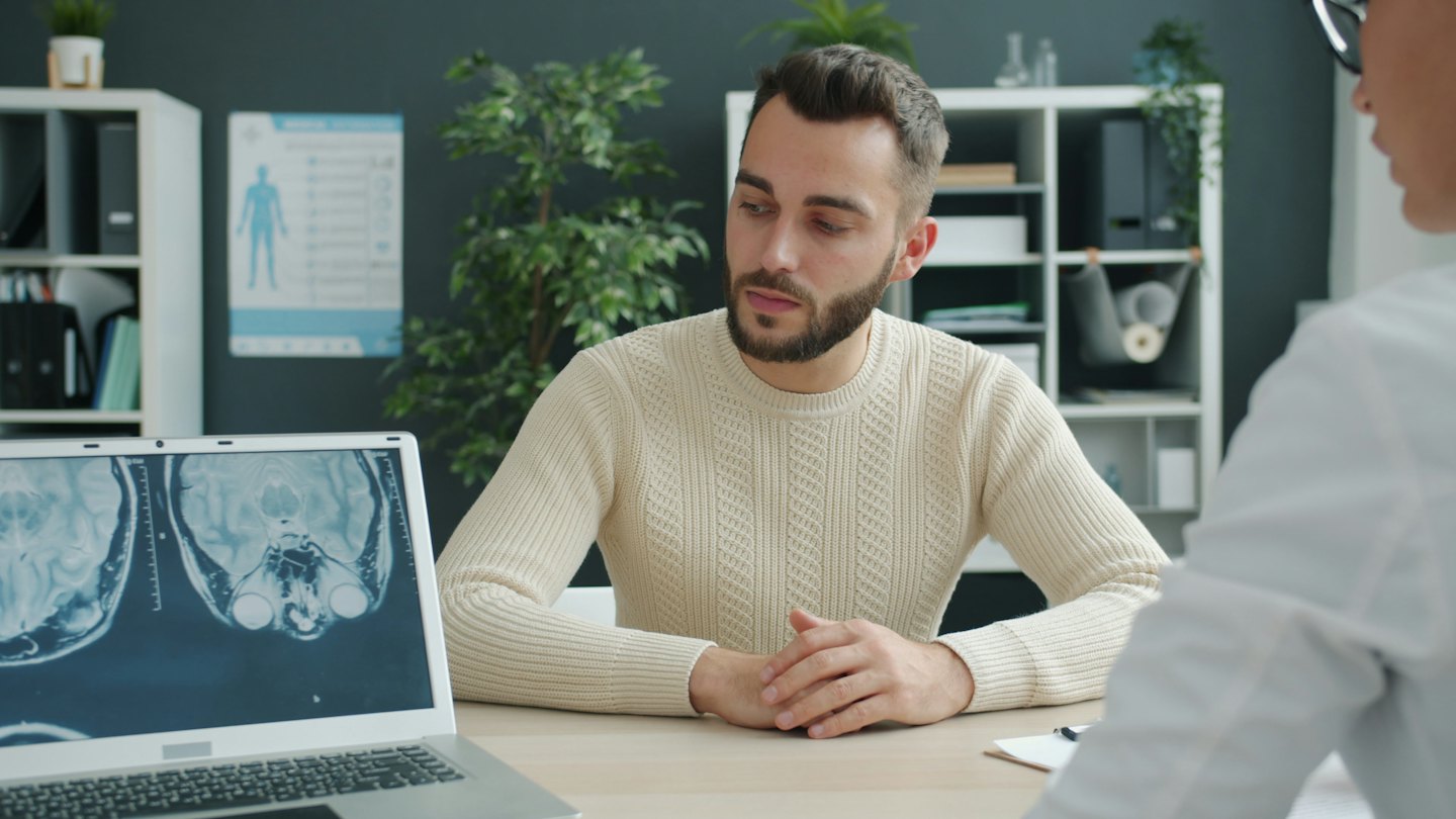 Läkare diskuterar resultat av hjärnskanning med patient via laptop.